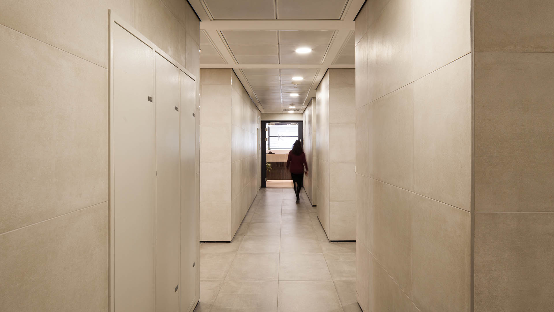 עיצוב מעברים ומסדרונות בקומות המבנה, שימוש בחיפוי אבן בגוון אופוויט בהיר ופרופיל ניתוק ברצפה.