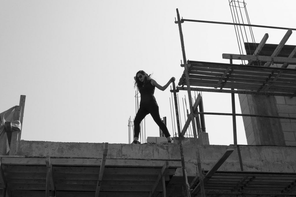 אדריכלית מיכל אהרוני גובס באתר בניה הולכת על קורה צילום בשחור לבן